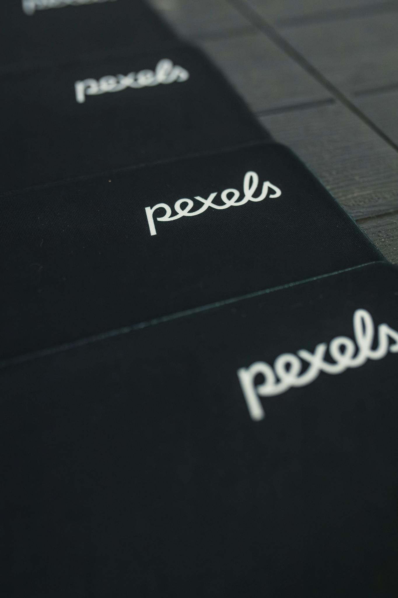 A close-up view of the Pexels logo displayed on a dark surface in a repeating pattern.